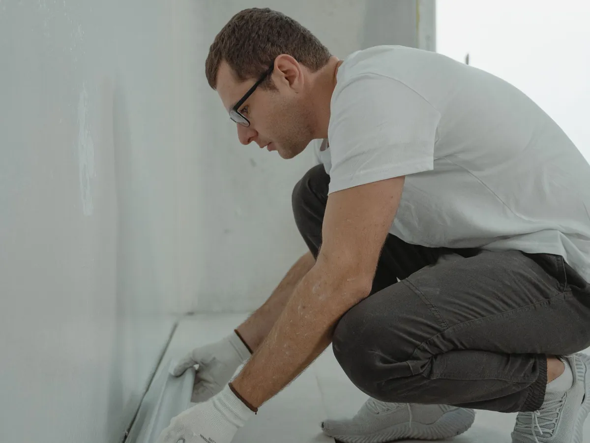 Artisan accroupi qui prépare un mur blanc pendant une rénovation intérieure