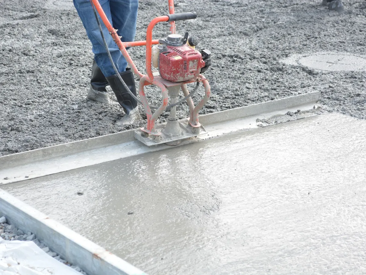 Ouvrier qui lisse une dalle de béton fraîchement coulée à la règle vibrante