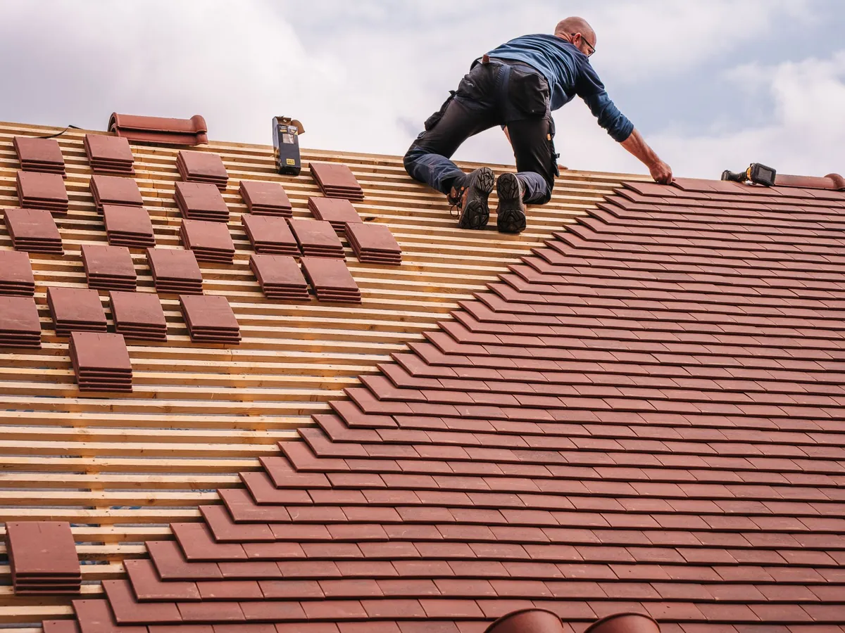 Couvreur qui pose des tuiles plates sur un toit en rénovation