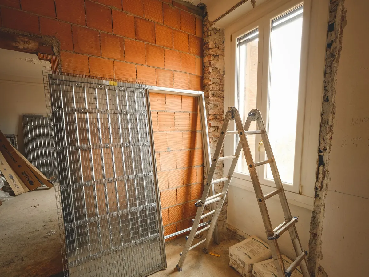 Pièce en rénovation avec échelle, matériaux et murs de briques