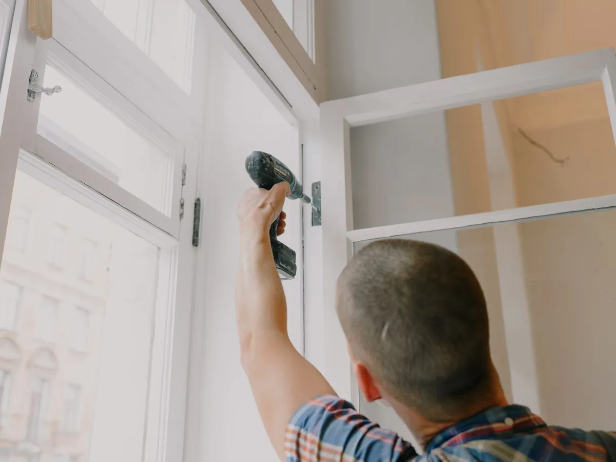Artisan qui visse une ossature à la perceuse dans une pièce en travaux