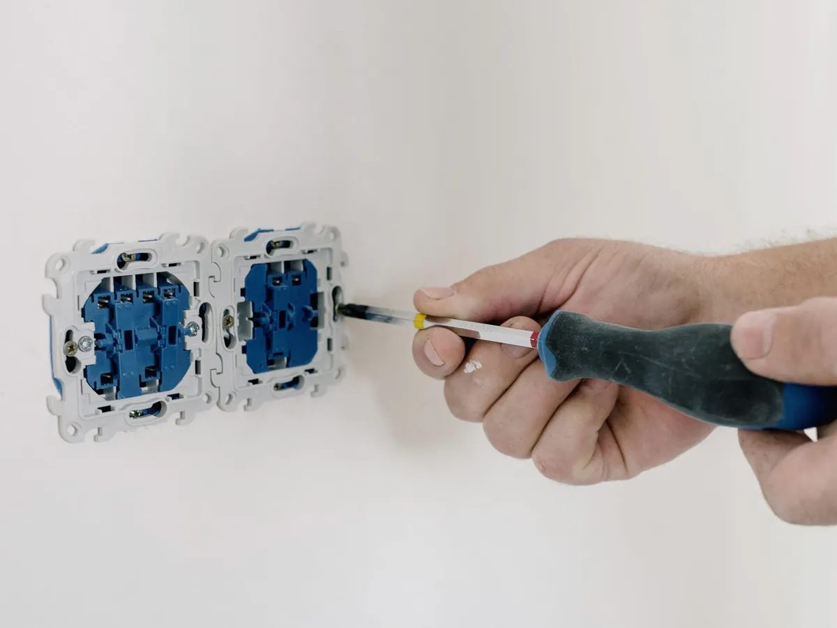 Électricien qui fixe une double prise murale avec un tournevis