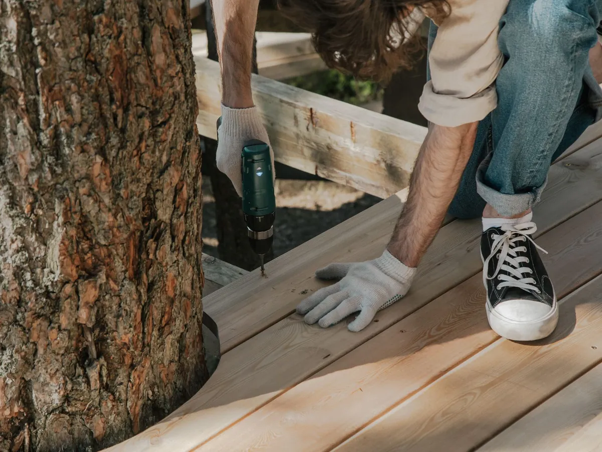 Artisan qui fixe les lames d'une terrasse en bois autour d'un arbre