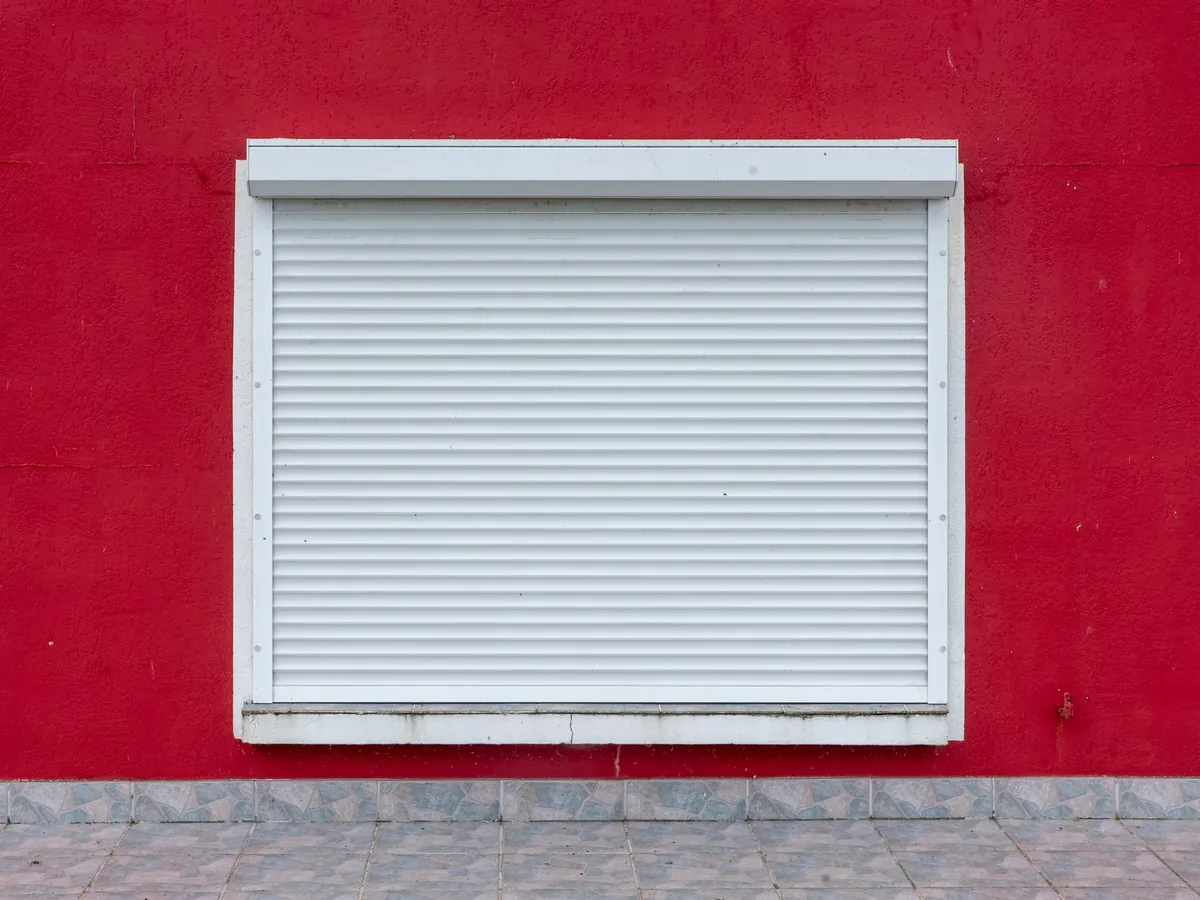 Volet roulant blanc à demi fermé sur une façade rouge